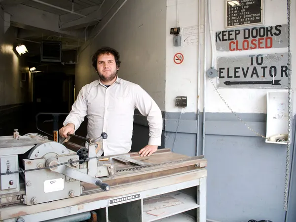 Ryan standing in front of a Vandercook proof press on the loading dock of the old shop