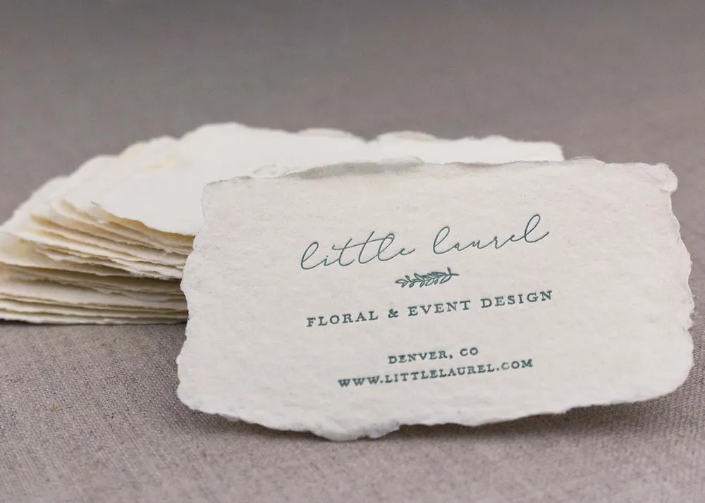 A stack of letterpress-printed business cards on handmade paper, showing varied deckled edges and visible fiber texture.